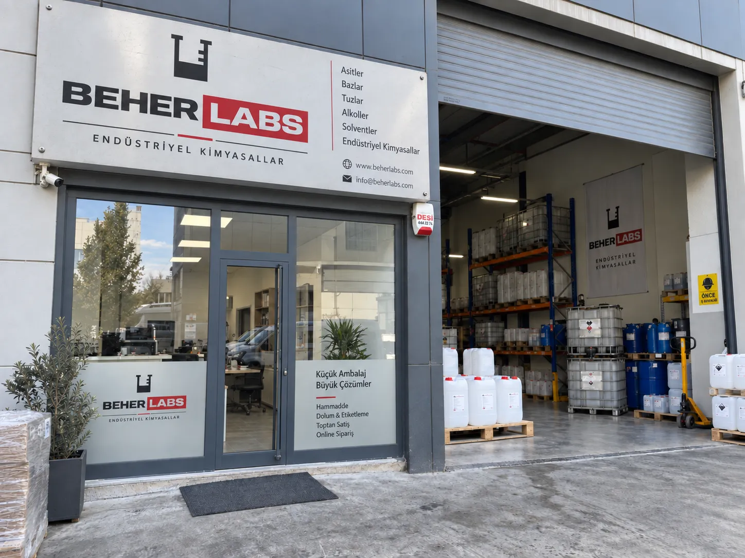 Office front with the company sign, beside the open warehouse door with racks of jerrycans and IBC totes